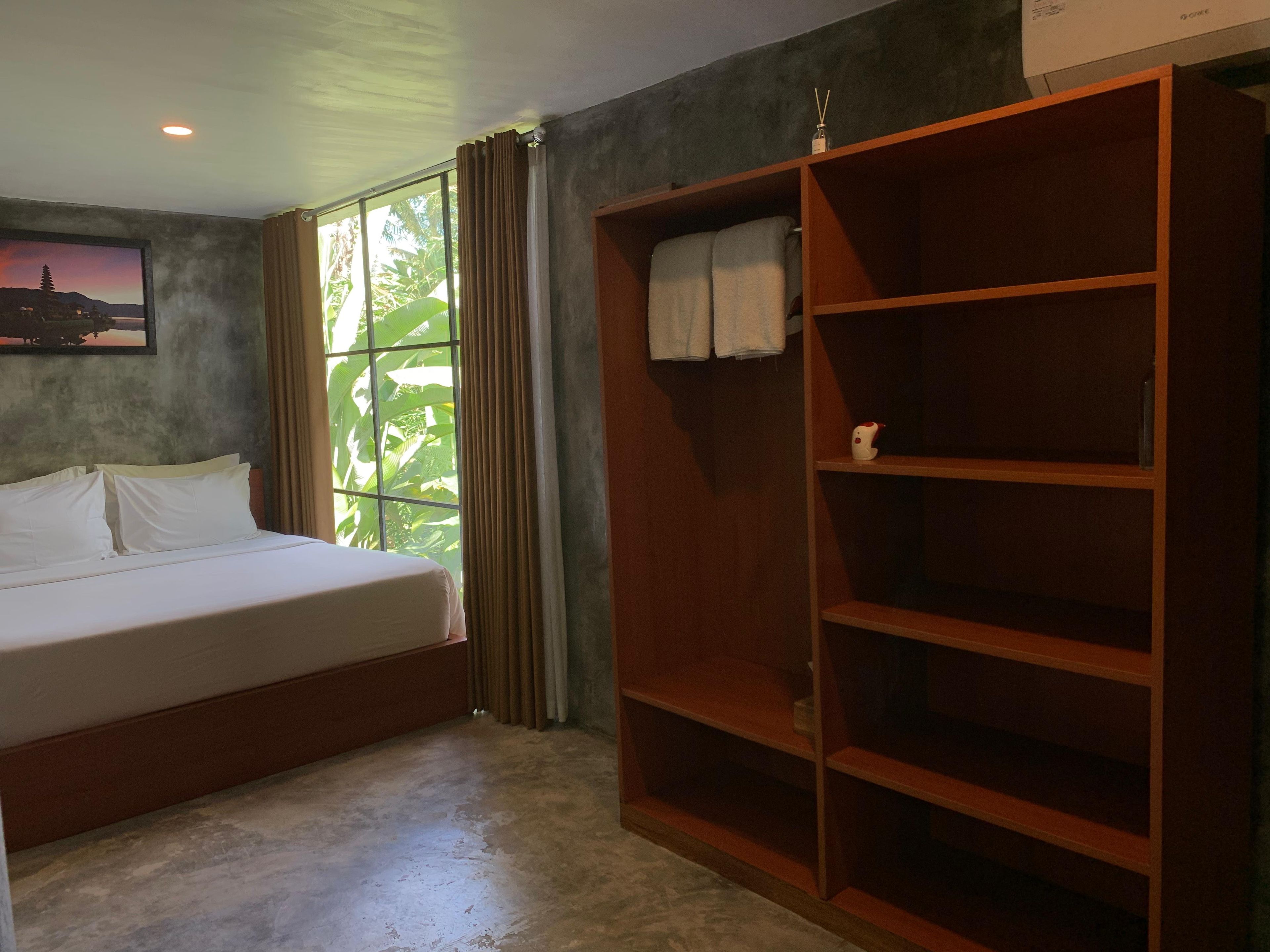 Un dormitorio con cama, ventana con cortinas, armario de madera y un cuadro en la pared.