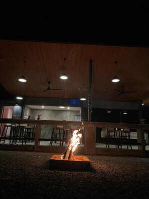 An indoor seating area with tables and chairs, a fire feature, ceiling fans, and a bar area.