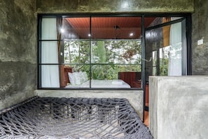 A room with a large window, a hammock, and a bed.
