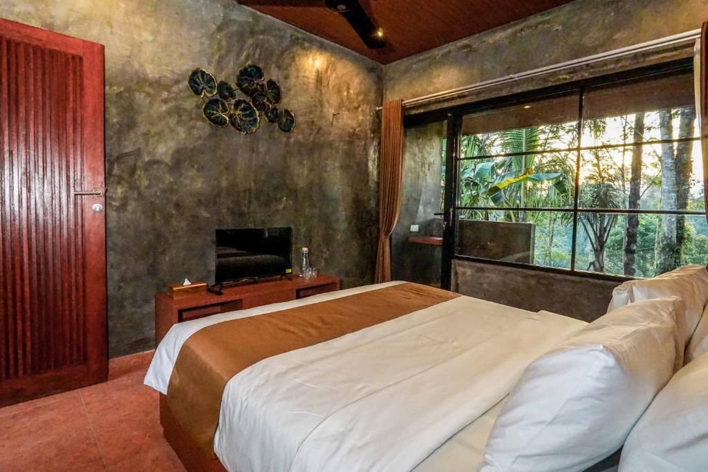 A bedroom with a bed, a television, a window with a view of trees, and a wooden door.