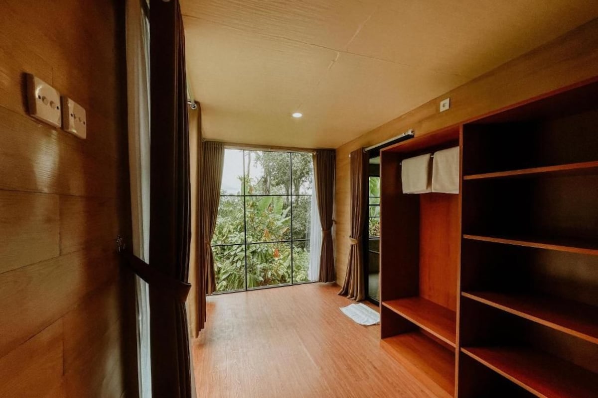 A room with a wooden floor, a large window with curtains, and a built-in wooden shelf unit.