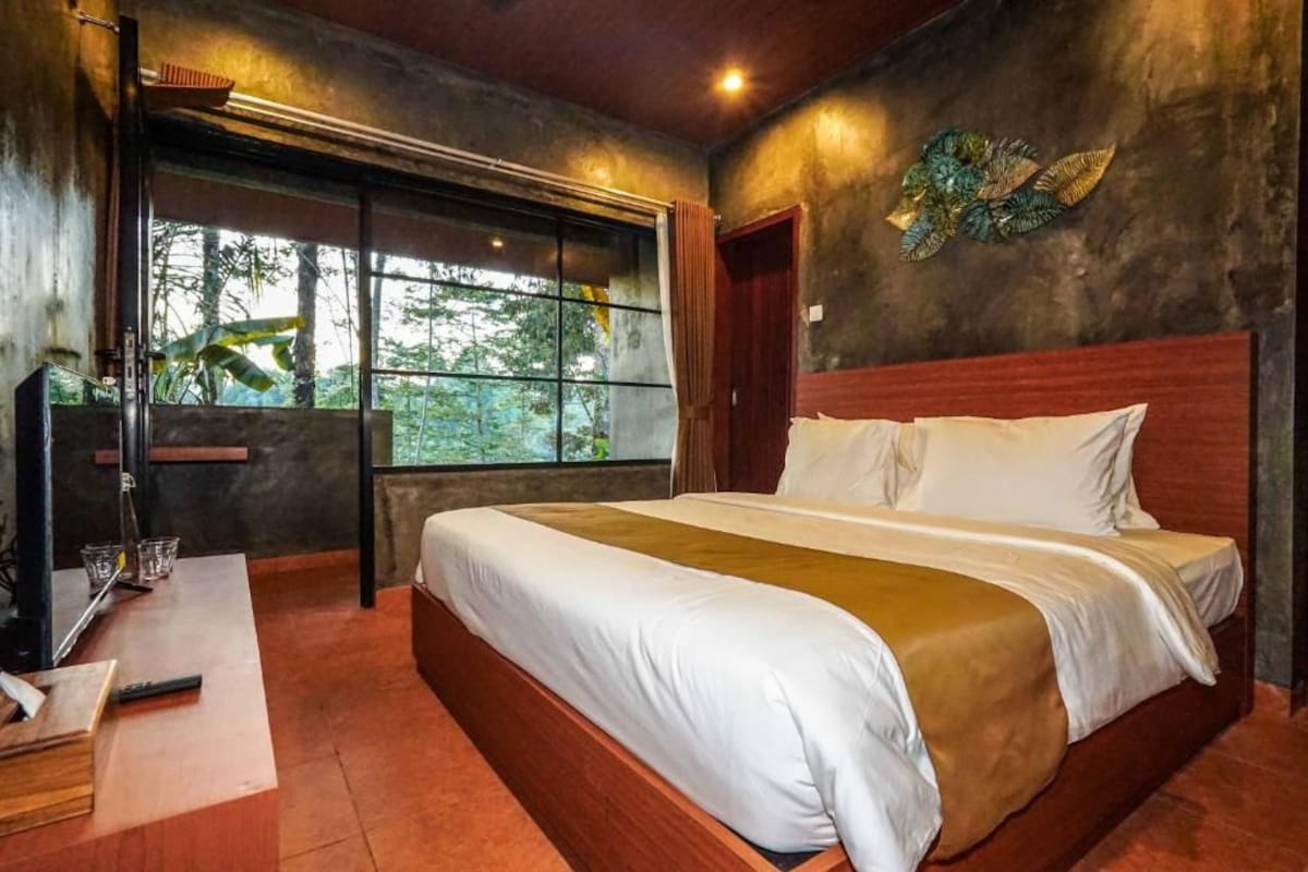 A bedroom with a large bed, a desk, and a window with a view of trees.