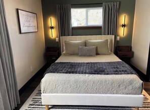Una camera da letto con un letto grande, due comodini, una finestra con tende e un punto luce a parete.