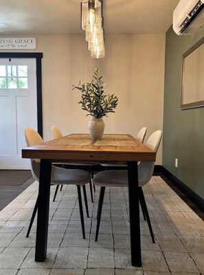 Una sala conferenze con tavolo in legno, quattro sedie, una pianta in vaso, una lampada a sospensione moderna e un condizionatore d'aria.