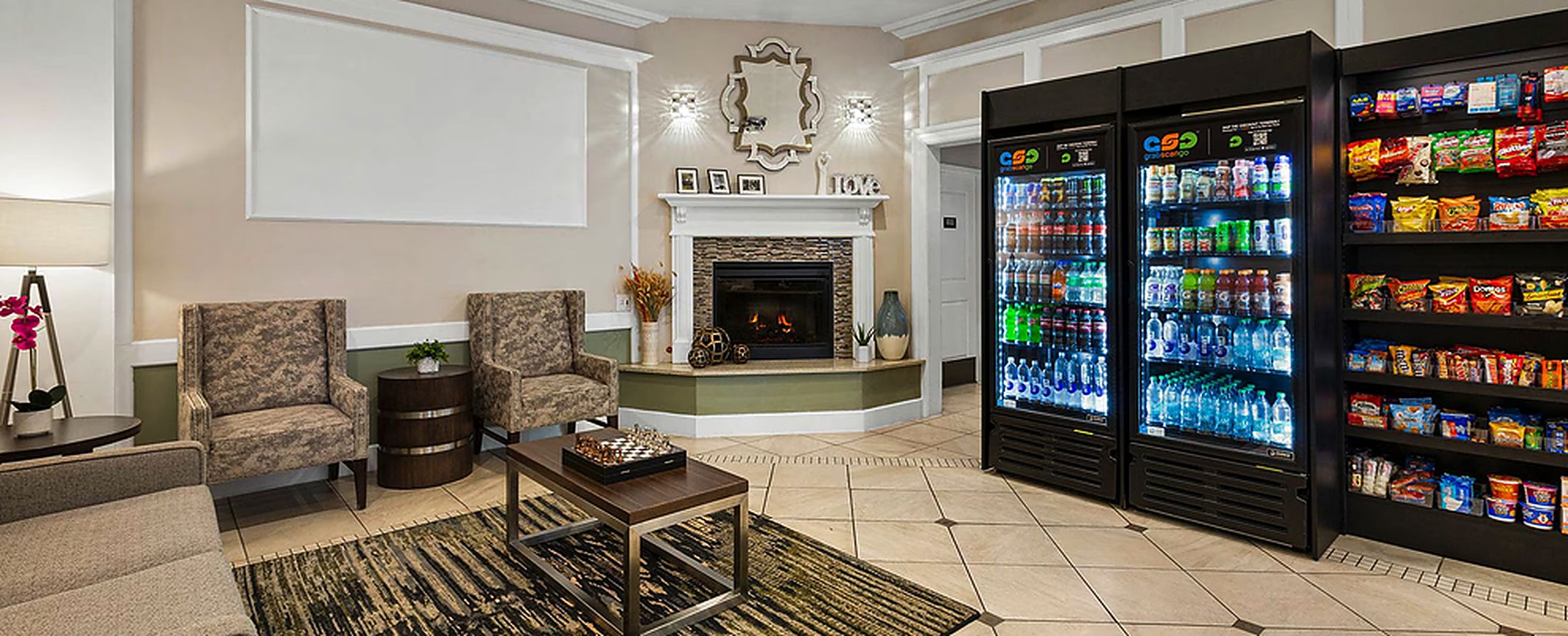 A living room with a fireplace, two armchairs, a coffee table, and a large beverage refrigerator.