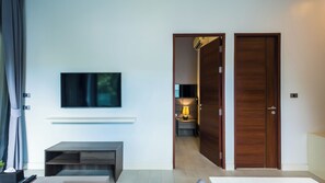 A modern living room with a flat-screen TV mounted on the wall, a wooden bench, and a door leading to another room. - Apartment 1 bedroom in Utopia (Mueang Phuket District)