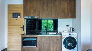 A compact kitchen with a microwave, sink, and washing machine, featuring a view of greenery through a window. - Apartment 1 bedroom in Utopia (Mueang Phuket District)