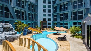 A hotel pool area with a slide, lounge chairs, and a view of the building's interior. - Apartment 1 bedroom in Utopia (Mueang Phuket District)