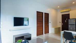 A modern living room with a flat-screen TV, a fireplace, a dining area with a table and chairs, and a kitchen with a refrigerator. - Apartment 1 bedroom in Utopia (Mueang Phuket District)