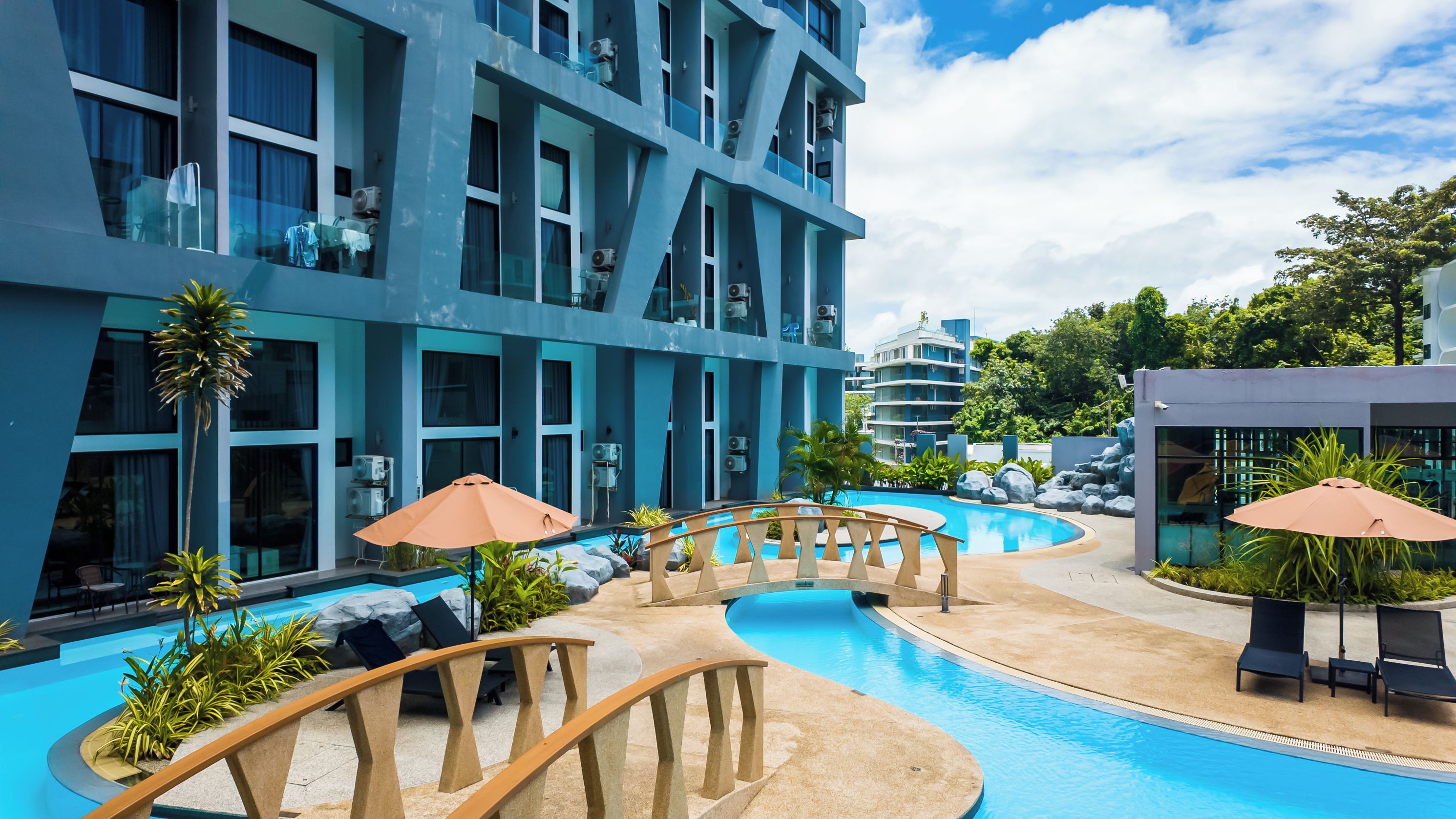 A modern hotel with a swimming pool, outdoor seating, and a view of the surrounding buildings.