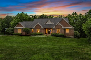 A two-story brick house with a gabled roof, a front porch, and a well-maintained lawn.