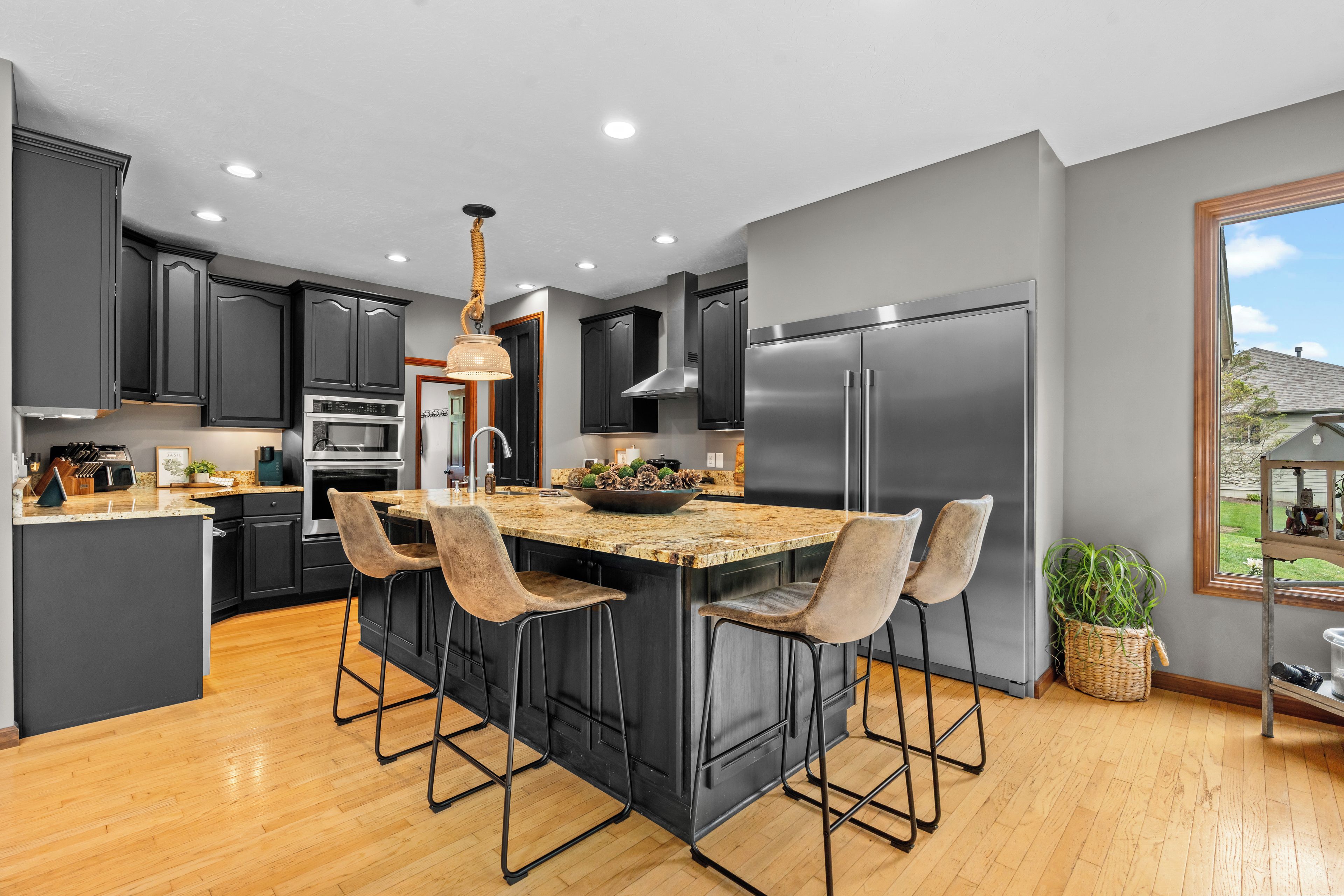 A modern kitchen with a central island, bar stools, stainless steel appliances, and a large window.