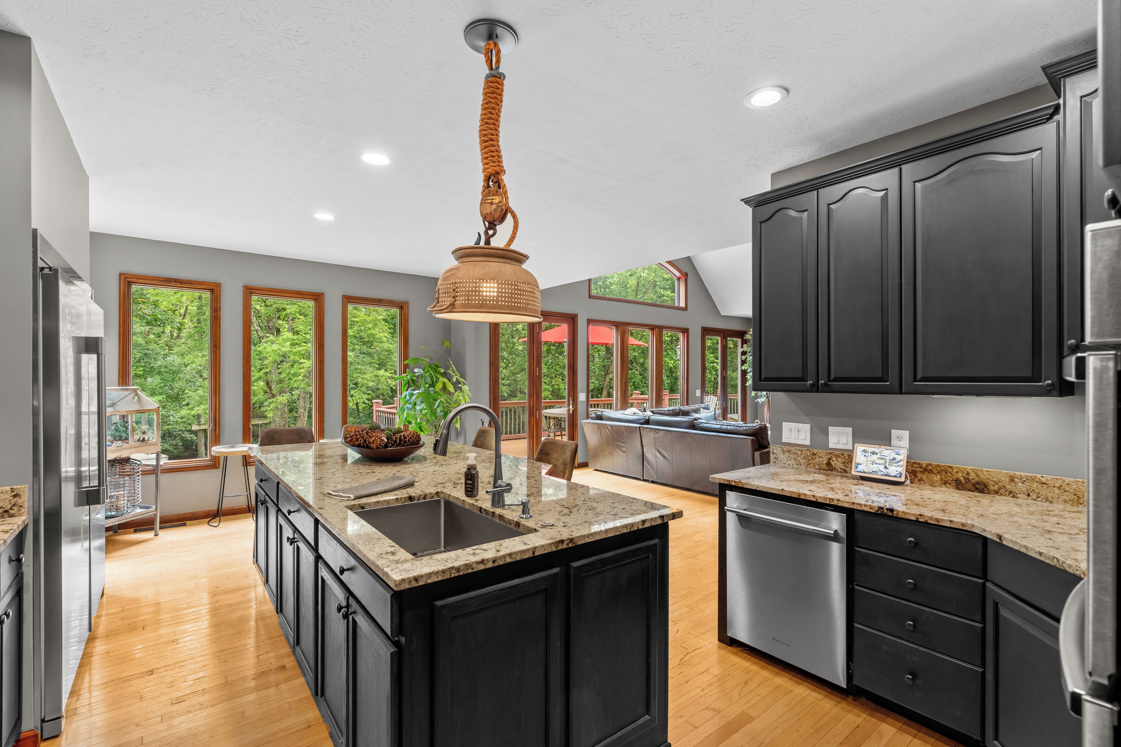 A modern kitchen with a central island, dark cabinetry, and a view of the outdoors through large windows.