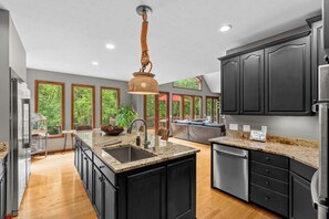 A modern kitchen with a central island, dark cabinetry, and a view of the outdoors through large windows.