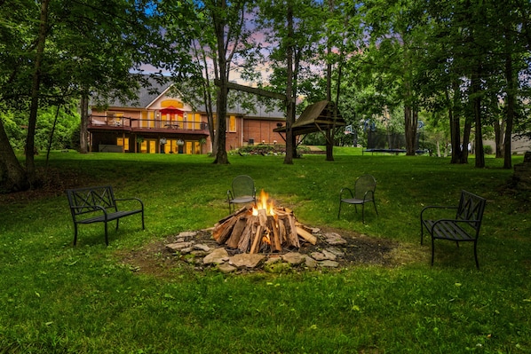 A backyard with a fire pit, outdoor seating, and a large house with a balcony.