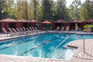 A swimming pool with lounge chairs and umbrellas, surrounded by trees. - Sunshine Getaway at Tuscana Resort (Davenport)