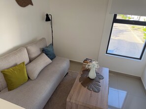 A living room with a sofa, a coffee table with a vase, a lamp, and a window with a view of the street. - Luxurious, fully furnished house (near the airport) in a central location with a pool and security features (Las Juntas)