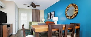 A hotel room with a dining table, chairs, a ceiling fan, a television, and a blue accent wall. - WorldMark Kona, one of the most beautiful spots on the Big Island! (Kailua-Kona)