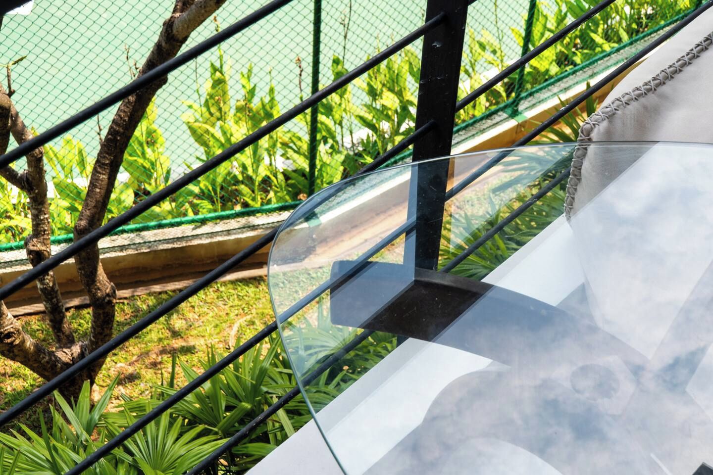 Un escalier extérieur moderne, doté de rampes en verre, entouré de verdure et délimité par une clôture métallique.