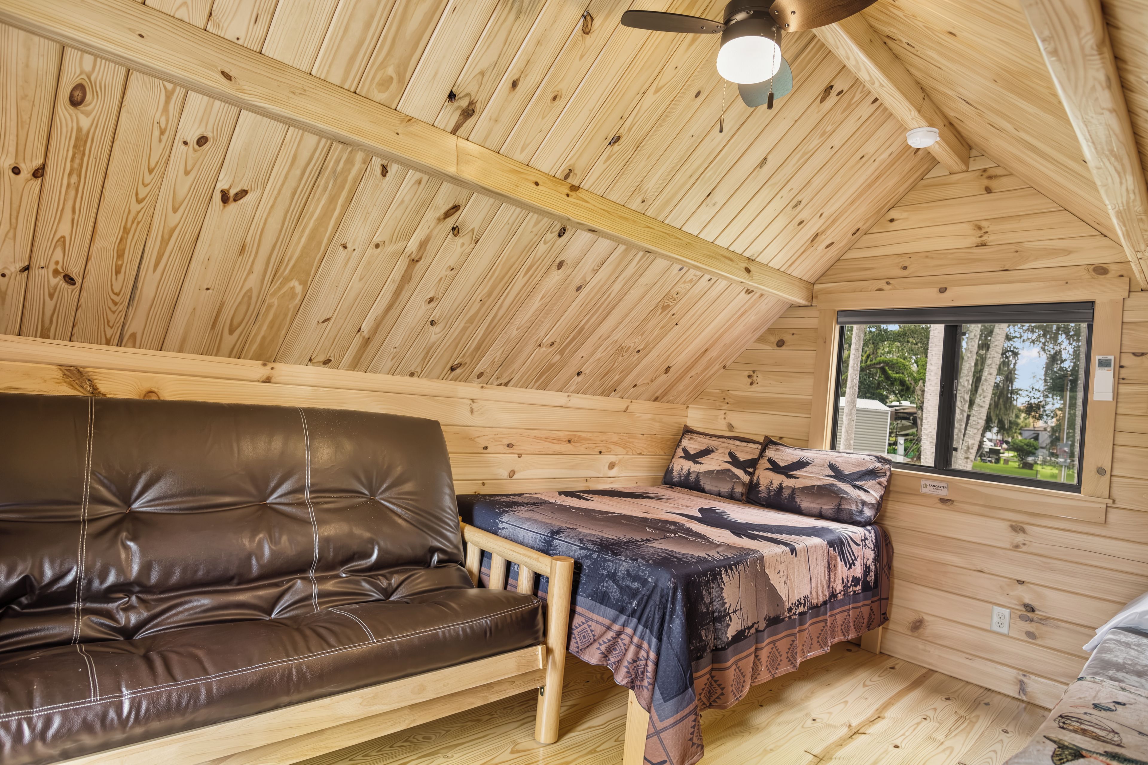 Cozy wood-paneled loft with futon, comfy bed, and peaceful tree views