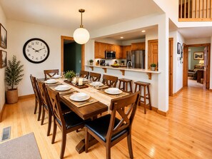 A dining area with a wooden table set for six, a clock on the wall, and a kitchen in the background. - 4BR Poconos Retreat, Fall at Camelback (Tannersville)