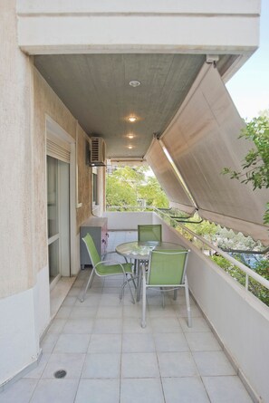 A balcony with a table and chairs, a window with blinds, and a view of greenery. - Casa  Luma (Marousi)