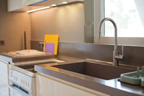 A modern kitchen with a stainless steel sink, a built-in oven, and a window providing natural light. - Casa  Luma (Marousi)