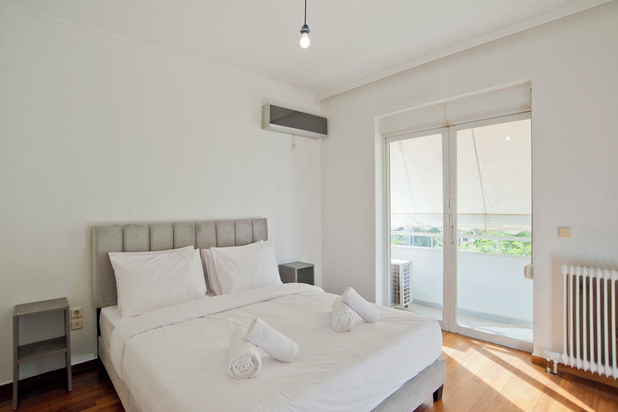 A bedroom with a bed, a nightstand, a radiator, and a window with a view.