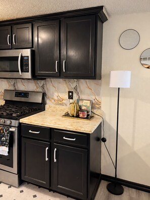 A kitchen with black cabinets, a microwave, a stove, and a countertop with a decorative item. - The Worldhouse: A Unique Travel-Themed Stay Near Seattle (Renton)