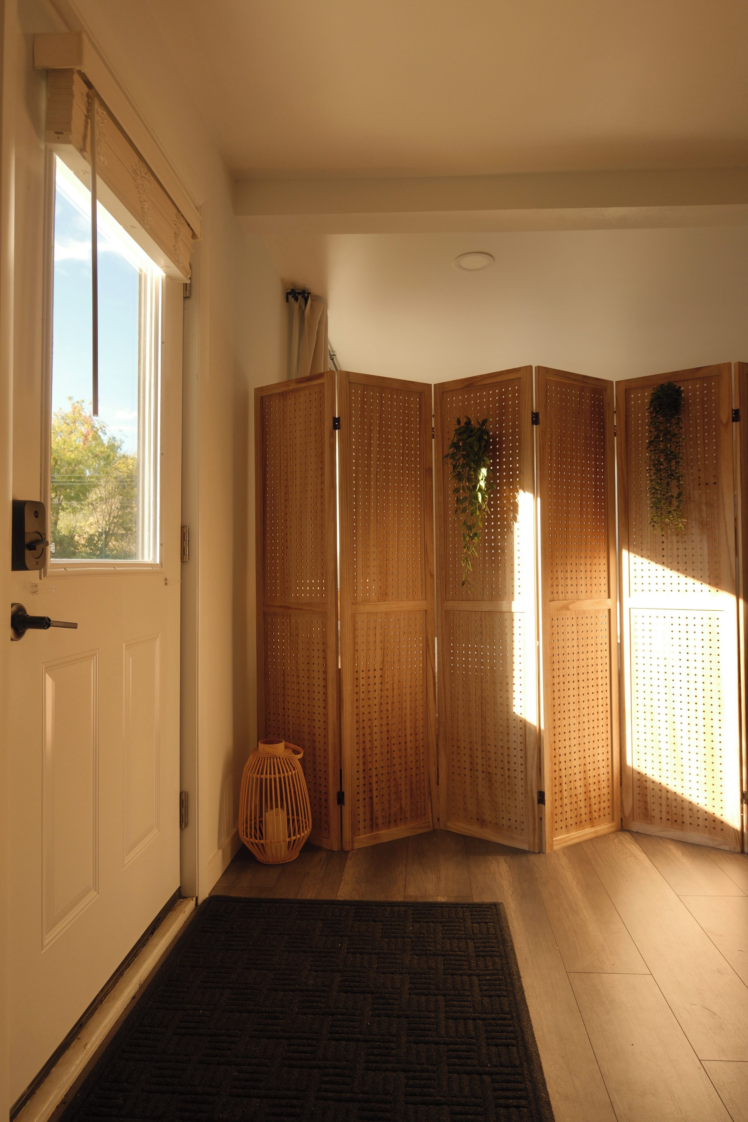 A room with a sliding wooden partition, a door with a handle, a small wicker basket, and a black rug on the floor.