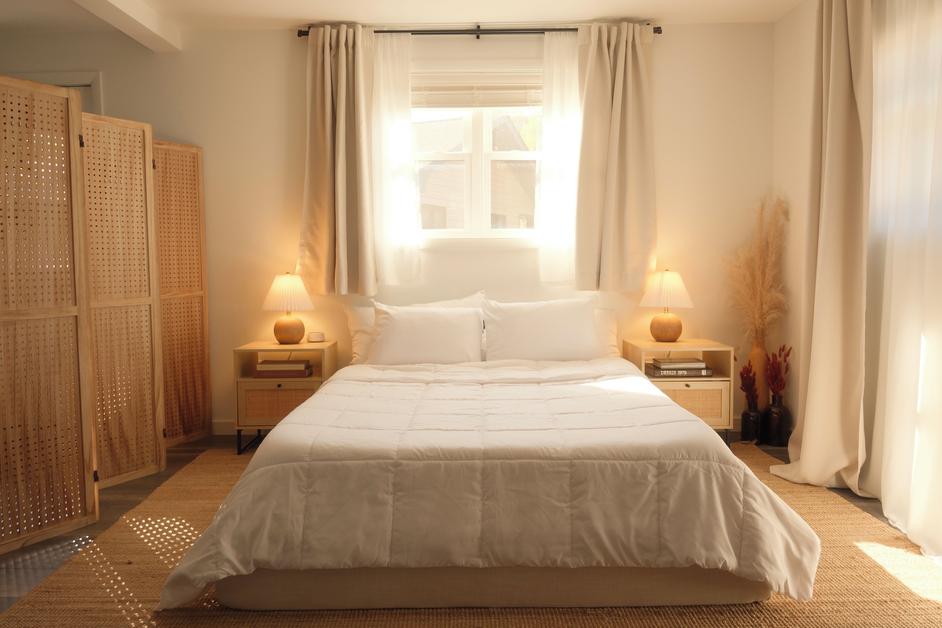 A bedroom with a large bed, two bedside tables, a window with curtains, and a wooden wardrobe.