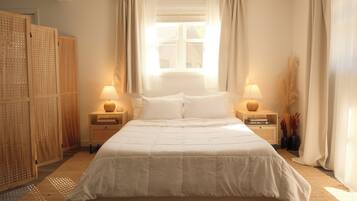 A bedroom with a large bed, two bedside tables, a window with curtains, and a wooden wardrobe.