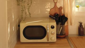 Eine Küche mit einer weißen Mikrowelle, einem Regal mit einem Radio und einem gerahmten Bild, einer Bierflasche und einer Topfpflanze.