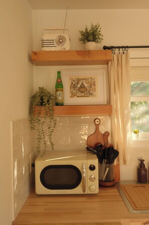 Cuina amb microones blanca, prestatge amb un aparell de ràdio i una fotografia emmarcada, una ampolla de cervesa i una planta en test.