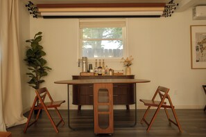 Un comedor con una mesa redonda, dos sillas, una planta en maceta y un ventanal con vistas a árboles.