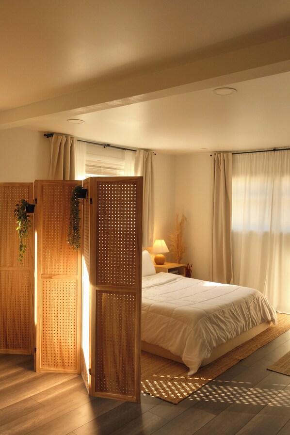 Un dormitorio con cama, mesita de noche, lámpara y un panel de madera con diseño perforado.
