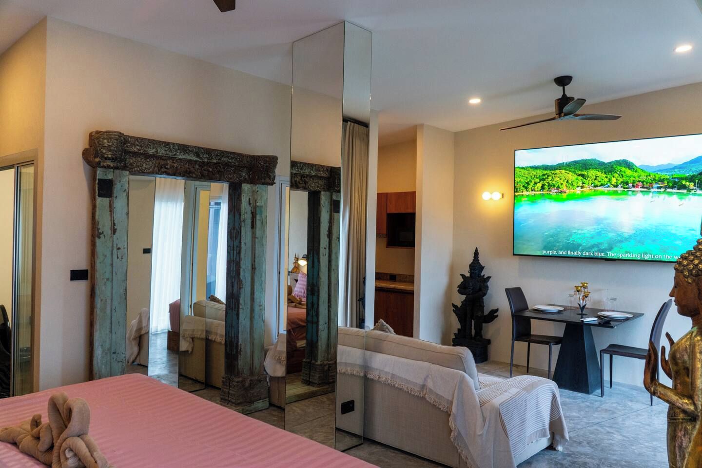 A hotel room with a bed, a dining table, a TV, and a large mirror.