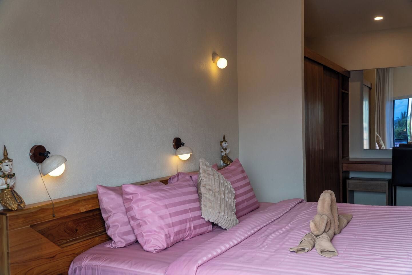 A hotel room with a bed, two wall-mounted lamps, a wooden headboard, and a window with a view.