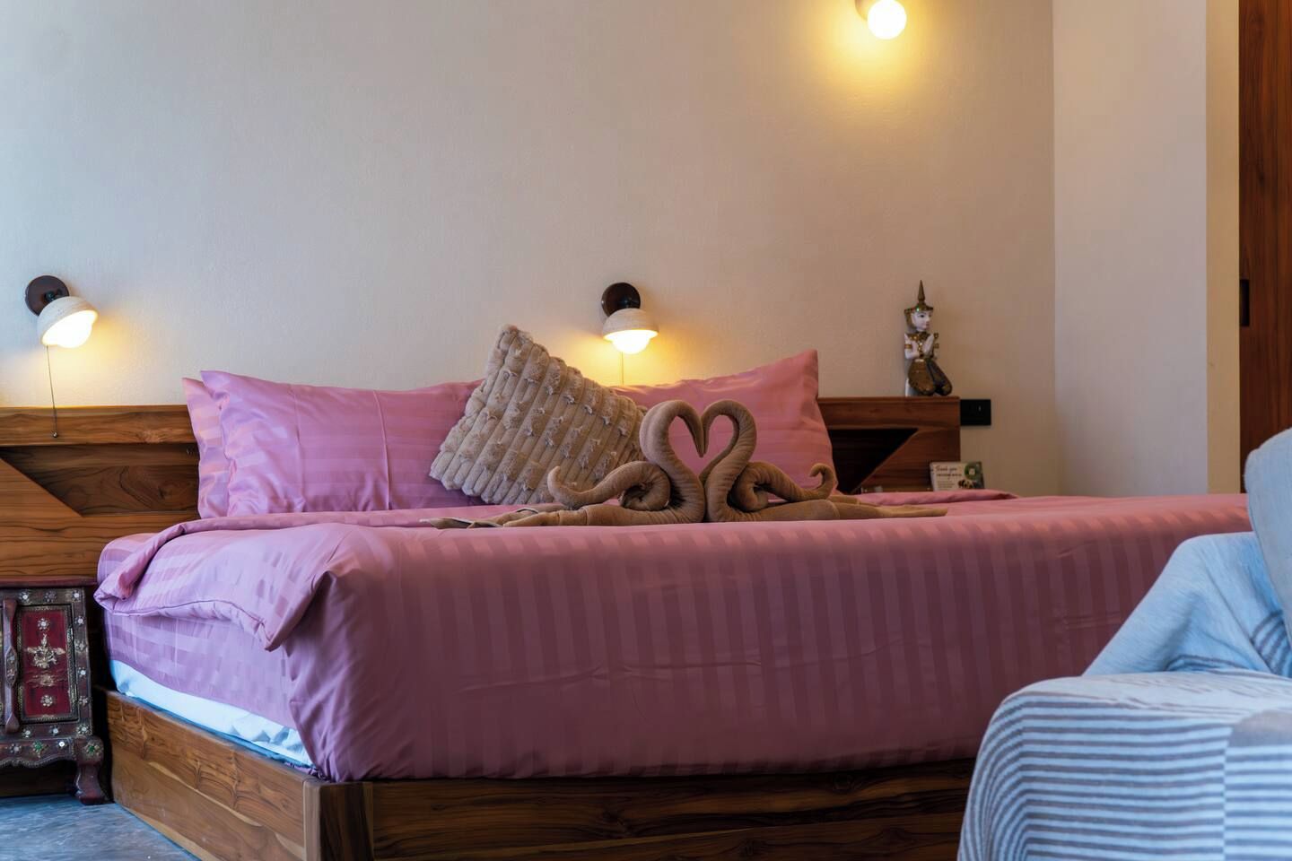 Un lit avec une literie rose, une tête de lit en bois et une disposition de serviettes en forme de cœur.