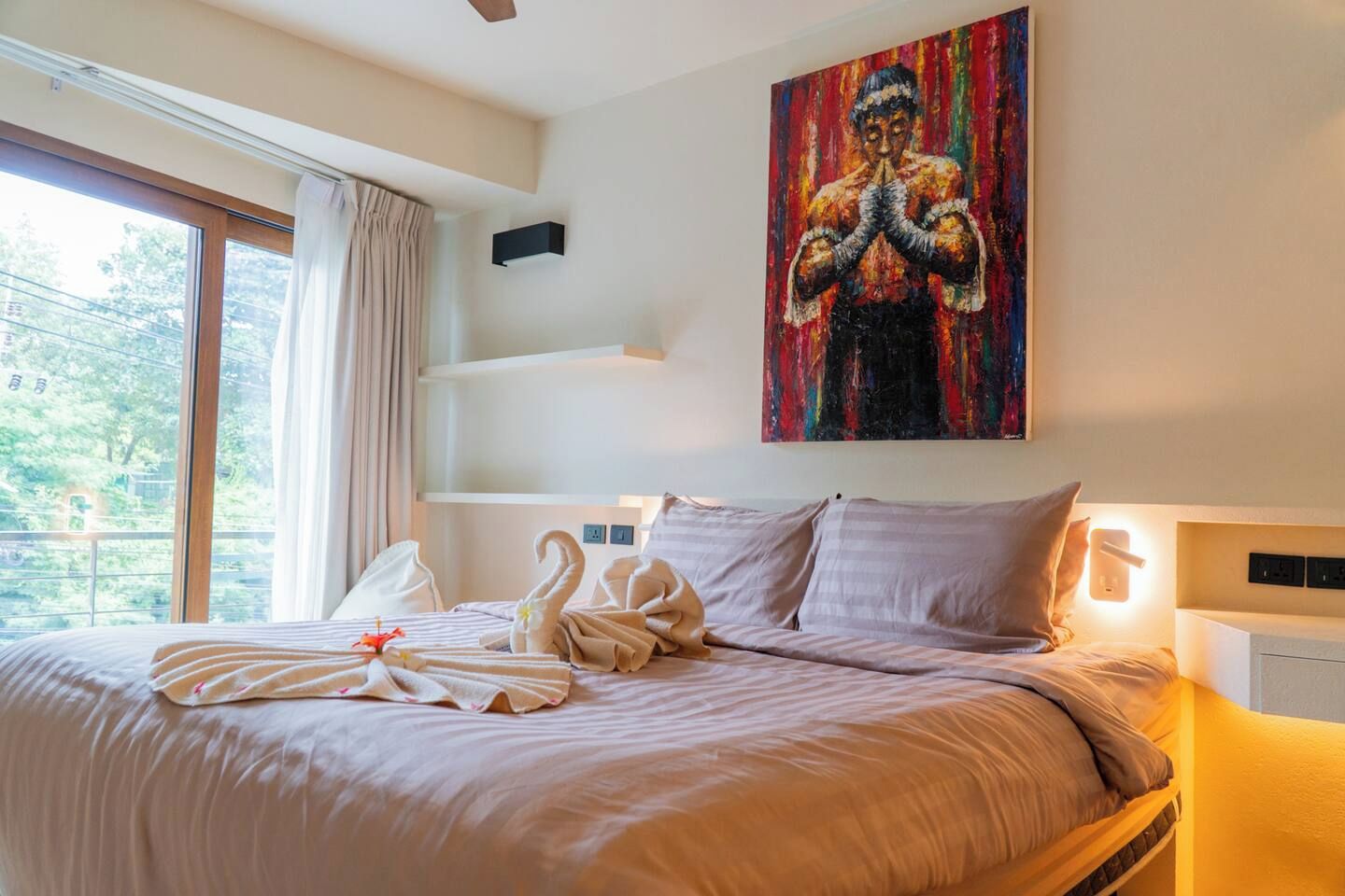 A hotel room with a bed, a painting, and a view of trees through the window.