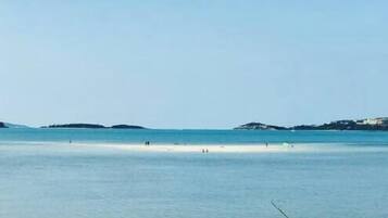 Een strand met kalm water, verre landschappen en een heldere lucht.