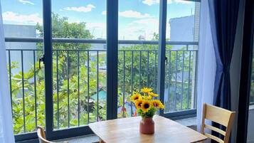 A room with a wooden table and chairs, a hanging light fixture, and large windows with a view of greenery.