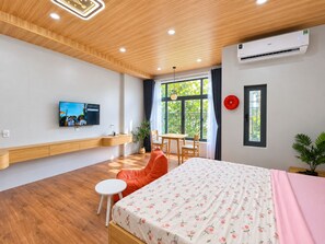 Une chambre d’hôtel moderne avec un plafond en bois, un téléviseur à écran plat fixé au mur, un lit recouvert d’une courtepointe à motifs floraux, une petite table ronde et une chaise.