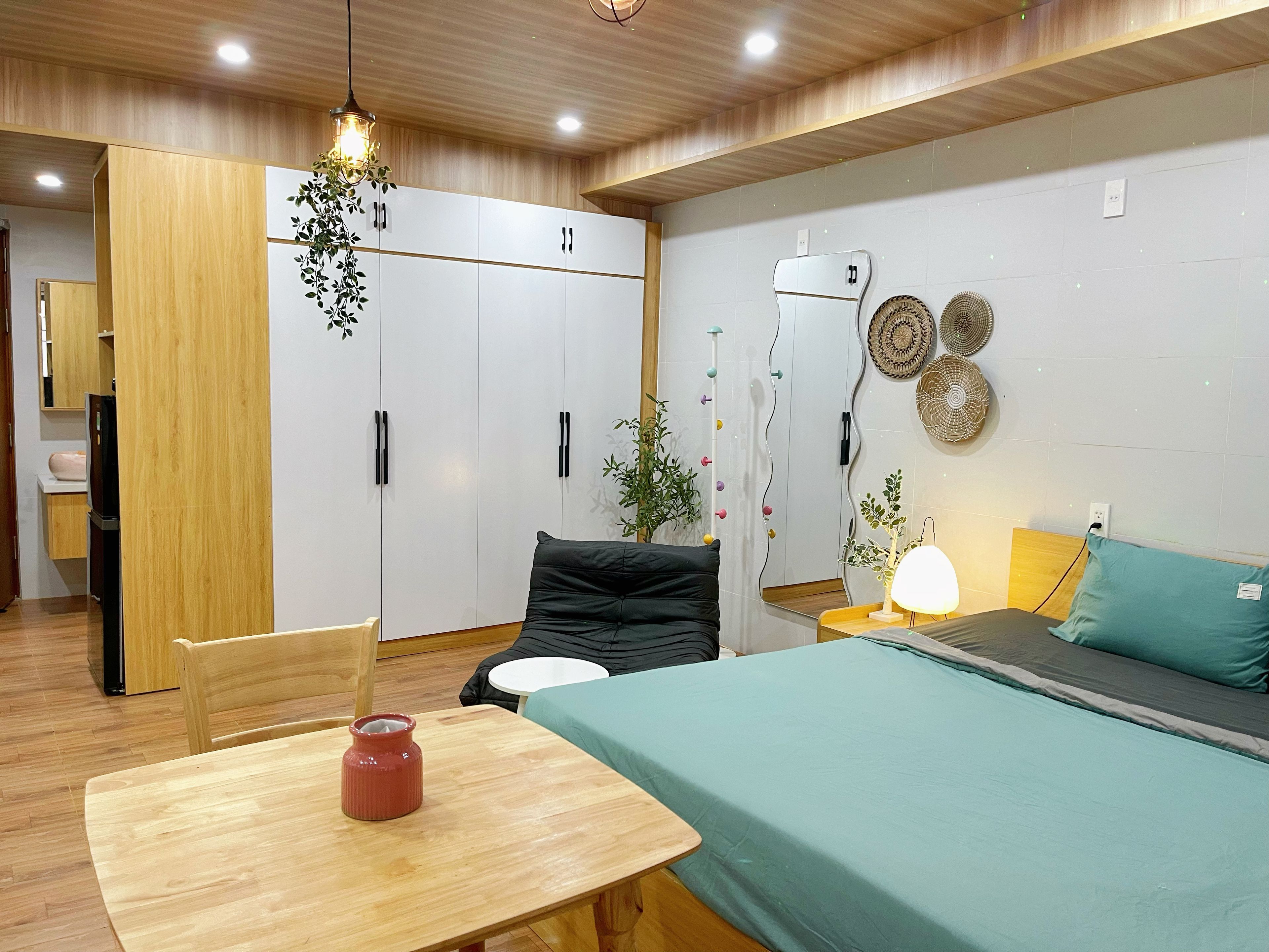 Un dormitorio moderno con una cama, mesita de noche y una silla. Hay un armario con espejo y una planta colgante.