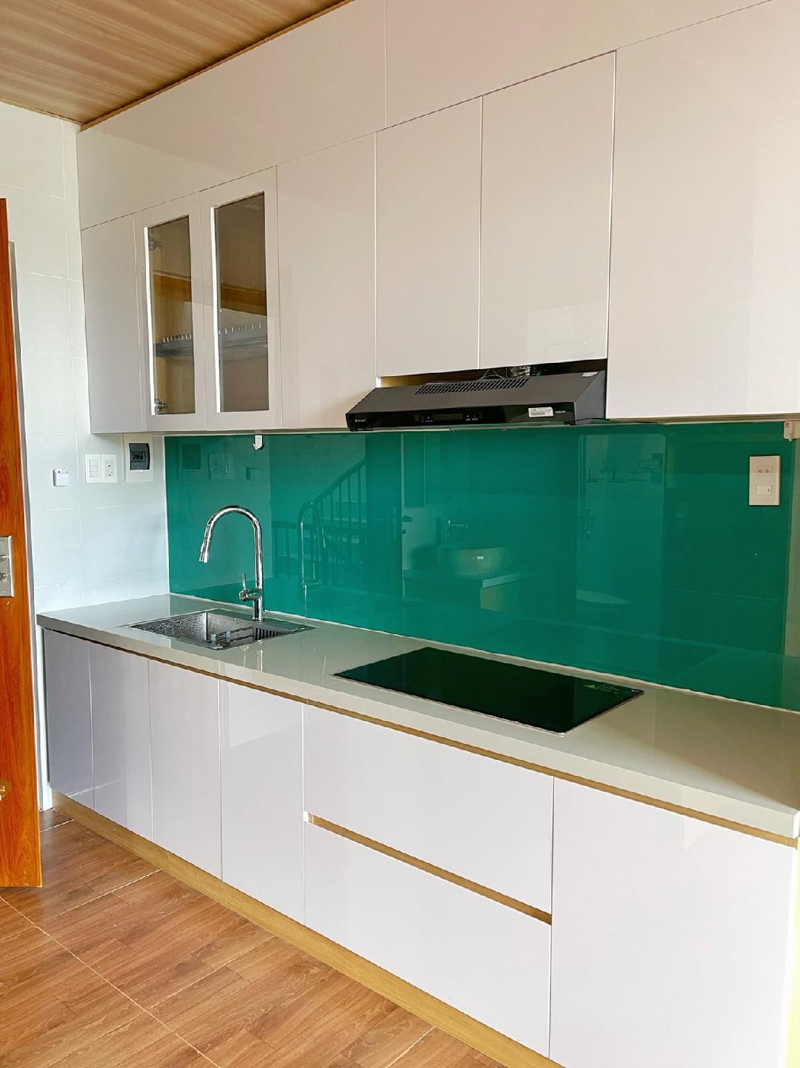 Una cocina moderna con armarios blancos, salpicadero verde y estufa integrada.