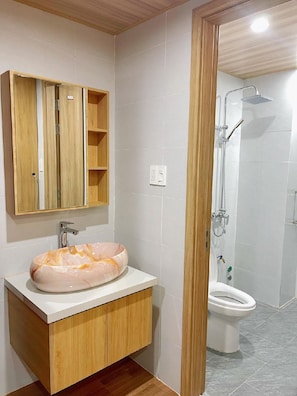 Un baño con tocador de madera, lavamanos de mármol, inodoro y cabina de ducha.