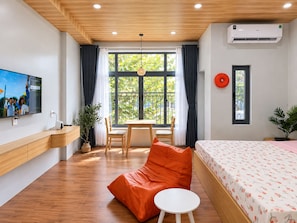 Habitación de hotel moderna con techo de madera, un ventanal con cortinas, una cama con colcha estampada, una mesita pequeña blanca y un televisor en la pared.