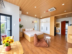 Une chambre moderne avec un plafond en bois, un lit recouvert d’une courtepointe à motifs floraux, une table de chevet, une commode, une plante en pot et une fenêtre donnant sur un beau paysage.