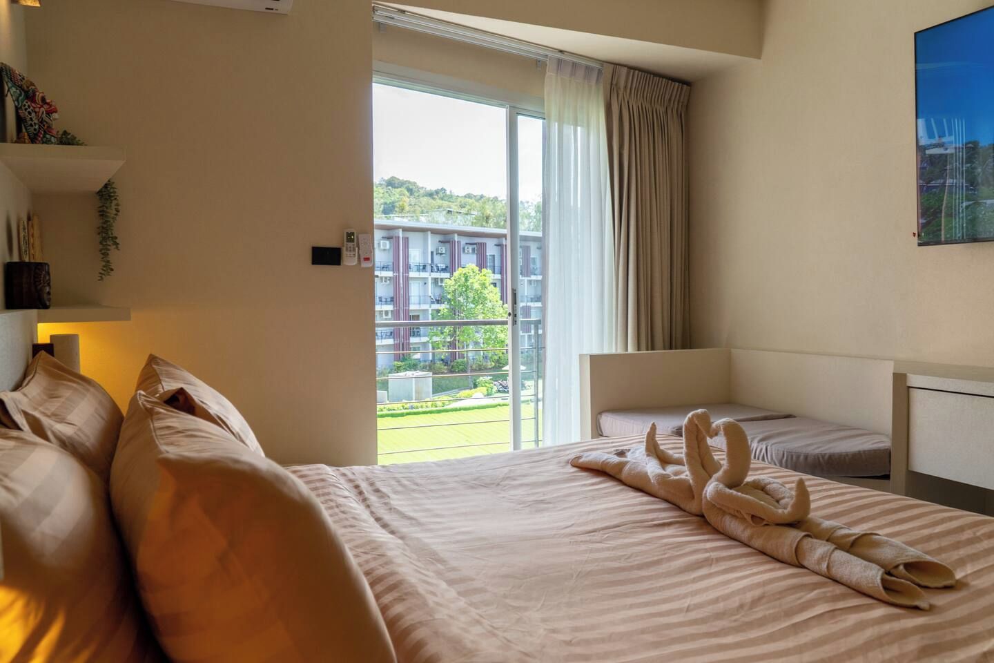 Een hotelkamer met een groot bed, een kleiner bed, een bureau en uitzicht op een gebouw en groen.