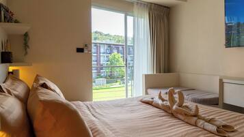 Een hotelkamer met een groot bed, een kleiner bed, een bureau en uitzicht op een gebouw en groen.